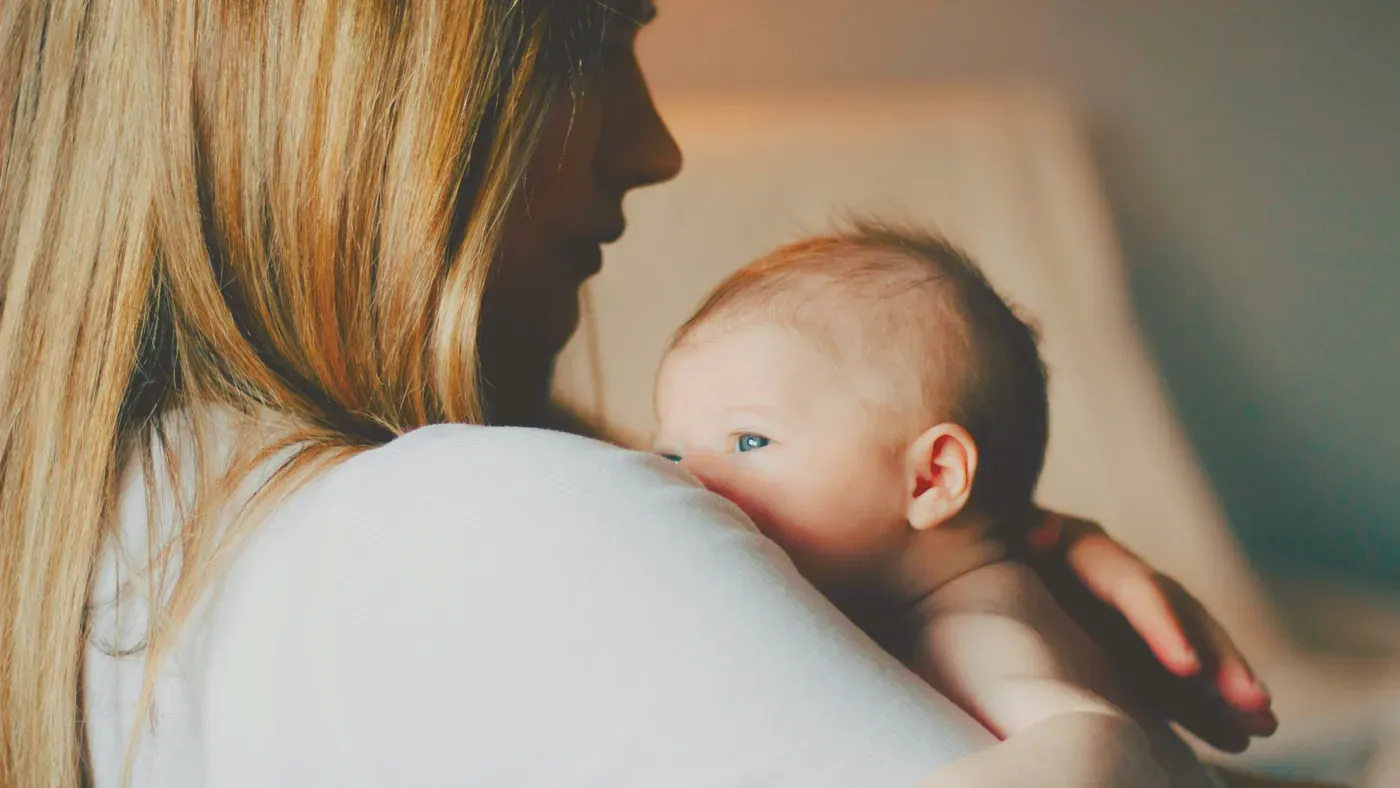 Nybliven mamma håller sin spädbarn mot axeln