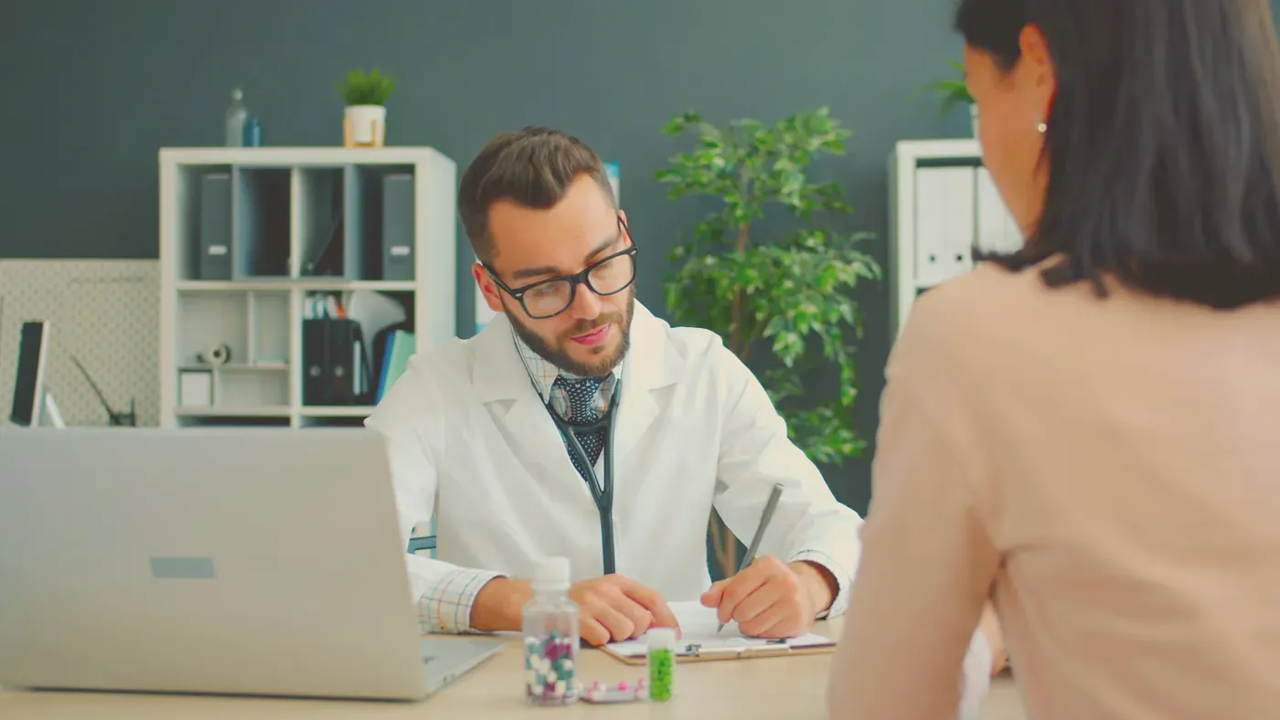 Läkare i vit rock samtalar med en kvinnlig patient vid ett skrivbord